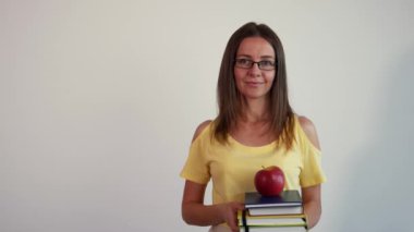 Kitap ve elma beyaz arka plan üzerinde tutan genç kadın. Öğretmen onun gözlük ayarlar. 