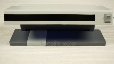 Dedektör ışık altında gerçek banknotlar arasında bir sahte banknot parlar.