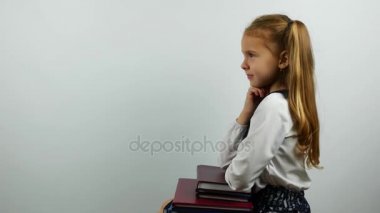 Üniformalı liseli kız dirsek kitap ve kameraya gülümseyen üzerinde oturur. Yan görünüm