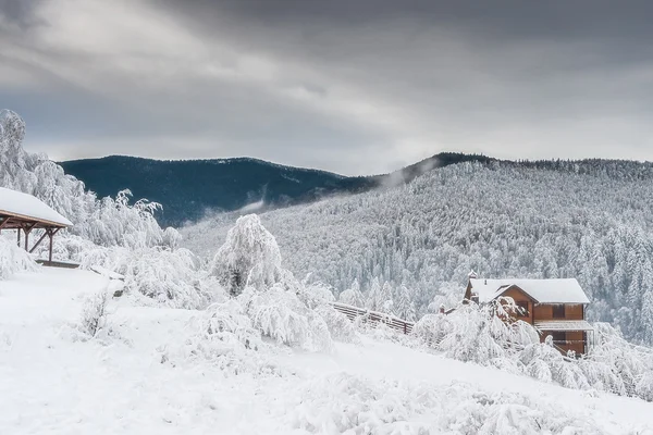 Bela paisagem de inverno com uma casa no fundo de florestas cobertas de neve e montanhas . — Fotografia de Stock