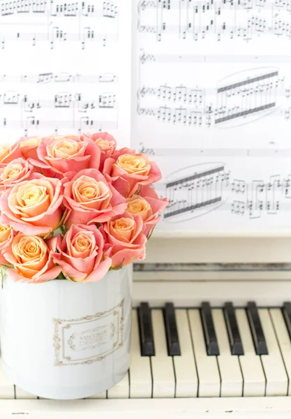 Beautiful pink roses in a round box on the piano.