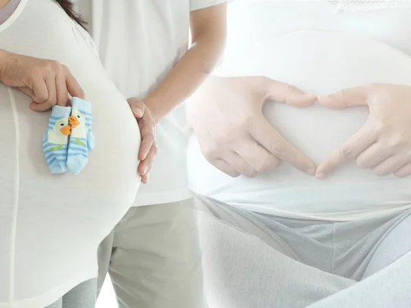 Gravid kvinna och hennes make som isoleras på vit bakgrund. Mamma håller nyfödda baby strumpor. Begreppet graviditet vård. Stockfoto