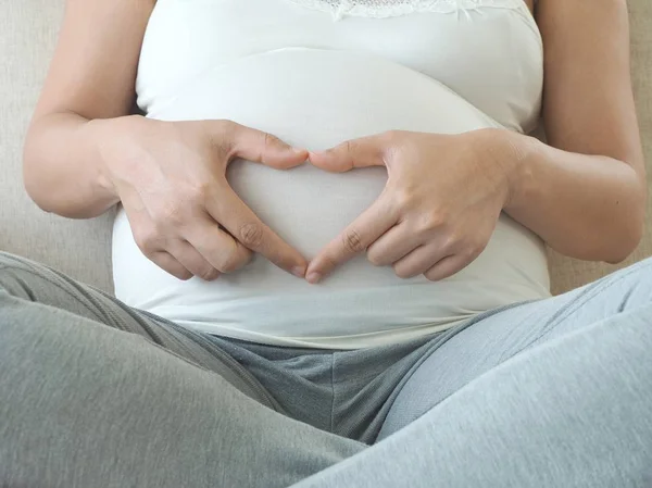Těhotná žena drží prsty ve tvaru srdce. Mateřská koncept a miminko. — Stock fotografie
