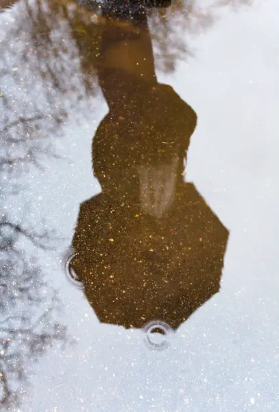 一个拿着伞的人被反映在水坑里. — 图库照片