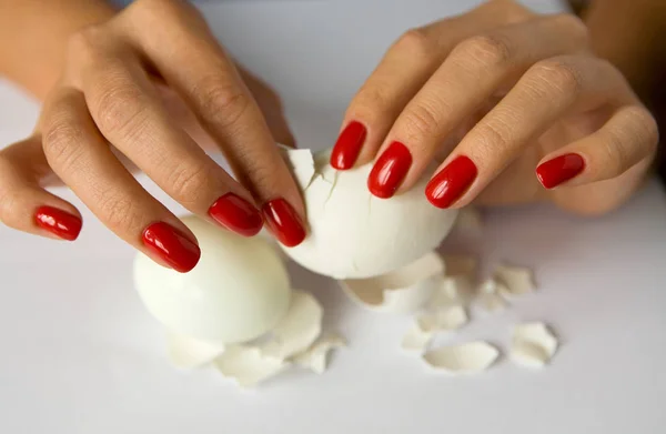 Female hands with a beautiful manicure clean the chicken egg. — Stock Photo, Image