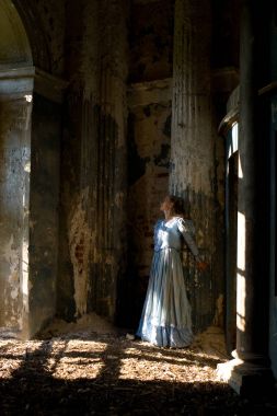 Ortaçağ elbiseli bir kız bir sütun duruyor.