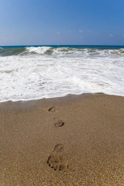 Human footprints lead from the raging sea.