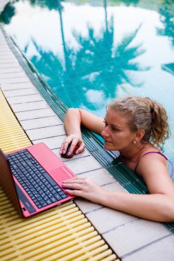 Bir kadın havuzda bilgisayarda çalışıyor.