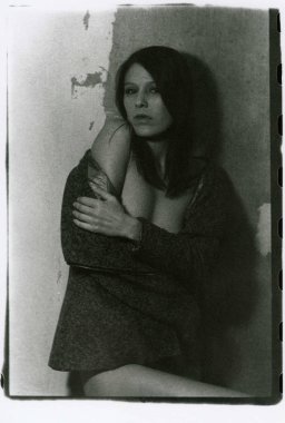 İnce, yarı çıplak bir esmer eski püskü bir duvarın yanında duruyor..