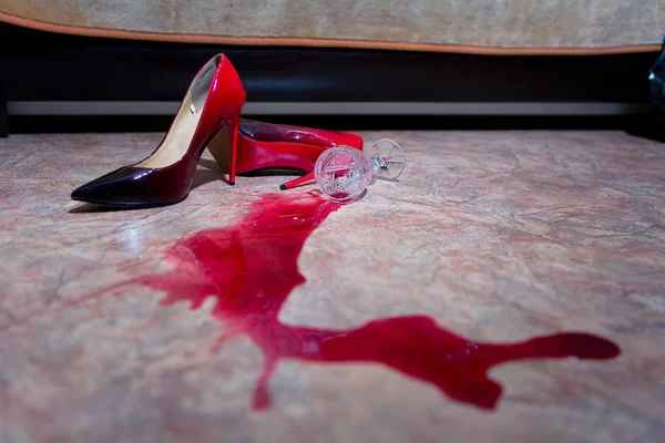 Una copa de vino derramada y zapatos de mujer en el suelo . Fotos de stock libres de derechos