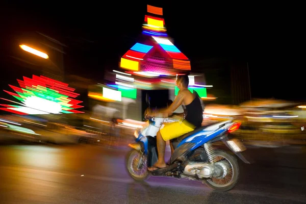 Um homem em uma motocicleta passa por edifícios brilhantes à noite . — Fotografia de Stock