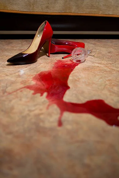Una copa de vino derramada y zapatos de mujer en el suelo . Fotos de stock