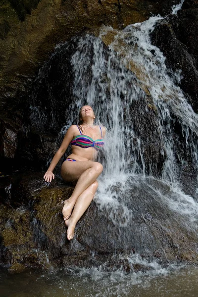 Die schöne schlanke junge Frau im Badeanzug sitzt auf einem Stein. — Stockfoto