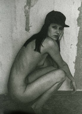 Beyzbol şapkalı çıplak bir esmer hırpalanmış bir duvarın yanında oturuyor..