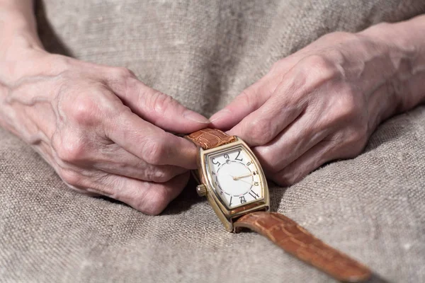 Las manos de una anciana sostienen un reloj de pulsera de cerca . Imagen de stock