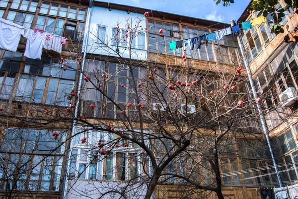 A typical georgian yard of an old traditional wooden house with persimmon tree and clothes and linen drying on the ropes. — Stock Photo, Image