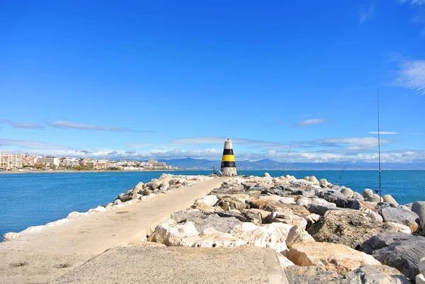 Uma vista para o mar Mediterrâneo, um farol com quebra-mares, varas de pesca de moradores locais e Torremolinos no fundo de um cais no porto de Benalmadena Puerto Marina, Andaluzia, Espanha . — Fotografia de Stock