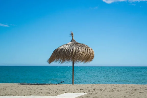Ένα ψάθινο ομπρέλα στην παραλία με τέλεια αμμουδιά και καταγάλανη θάλασσα σε Τορρεμολίνος (Επαρχία Μάλαγα, Ανδαλουσία, Ισπανία). — Φωτογραφία Αρχείου