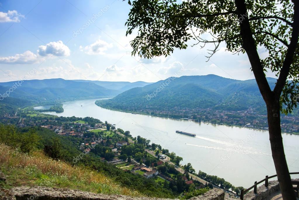 A view from the hill of Visegrad castle to Danube river and a ship, villages and mountains, with a tree at foreground, Visegrad, Hungary.