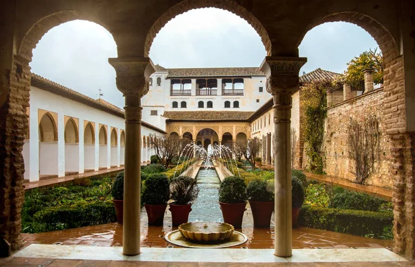 Granada, Spanien - 10. Februar 2015: ein Torbogen zum Innenhof mit Brunnen und geschnittenen Pinseln in den Gärten des Alhambra-Palastes, Granada, Andalusien, Spanien. — Stockfoto