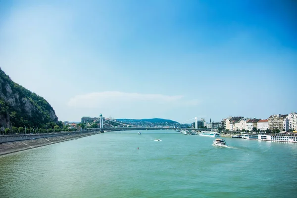 En vy till Donau floden, fartyg och vallar från ett bron i Budapest i centrera av staden, Ungern. — Stockfoto