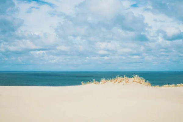 Sand dunes covered with dry grass and blue Baltic sea water at t
