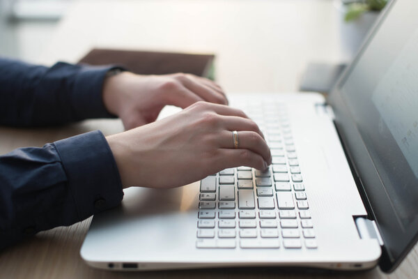 Hands typing on a laptop keyboard. A man works in an office at his workplace