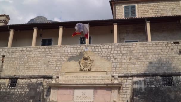 Kotor, Montenegró. A nemzeti montenegrói zászló és a város zászlója a régi város bejárata felett lebeg. — Stock videók