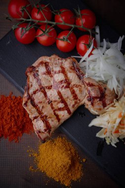 Çeşitli sebze ve baharat karanlık bir arka plan üzerinde ızgara domuz eti biftek.
