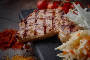 Çeşitli sebze ve baharat karanlık bir arka plan üzerinde ızgara domuz eti biftek.