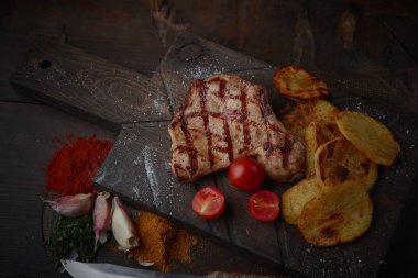Çeşitli sebze ve baharat karanlık bir arka plan üzerinde ızgara domuz eti biftek.
