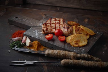 Çeşitli sebze ve baharat karanlık bir arka plan üzerinde ızgara domuz eti biftek.