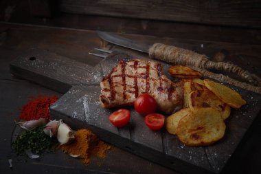 Çeşitli sebze ve baharat karanlık bir arka plan üzerinde ızgara domuz eti biftek.