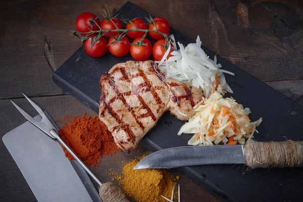 Çeşitli sebze ve baharat karanlık bir arka plan üzerinde ızgara domuz eti biftek.