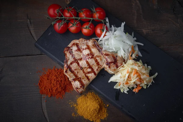 Çeşitli sebze ve baharat karanlık bir arka plan üzerinde ızgara domuz eti biftek.