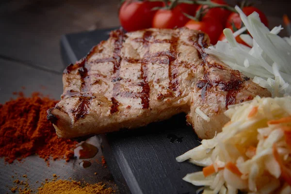 Çeşitli sebze ve baharat karanlık bir arka plan üzerinde ızgara domuz eti biftek.