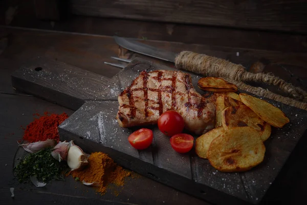 Çeşitli sebze ve baharat karanlık bir arka plan üzerinde ızgara domuz eti biftek.