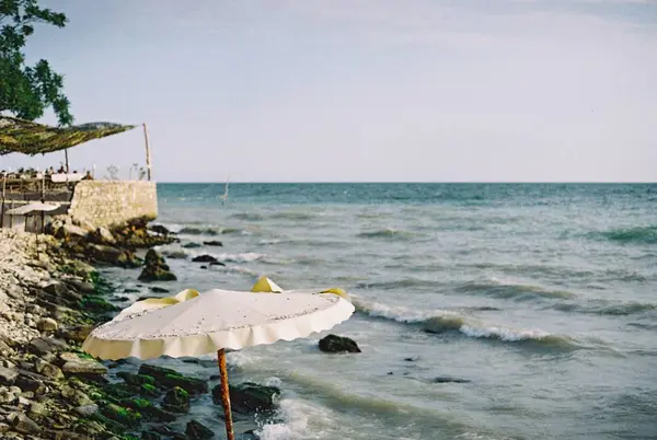 Летний День Скалистом Пляже Белым Зонтиком Размытыми Людьми Заднем Плане — стоковое фото