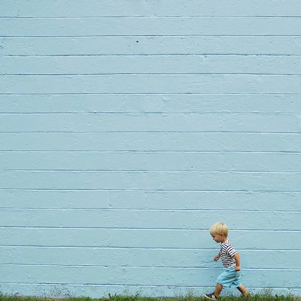 Chłopiec Chodzenie Trawniku Przed Murem Niebieski — Zdjęcie stockowe