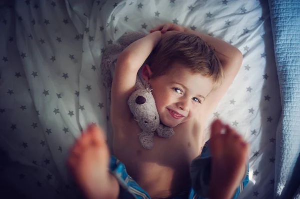 Хлопчик лежить на ліжку з приємною іграшкою — стокове фото