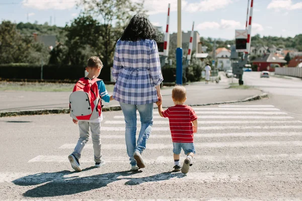 Mãe segurando seus filhos e atravessando uma estrada a caminho da escola — Fotografia de Stock