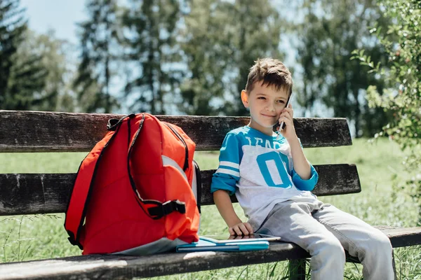 Un écolier fait une pause sur un banc et passe un coup de fil — Photo