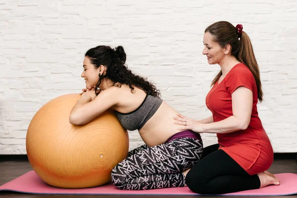 Parteira massageando uma mulher grávida enquanto se exercita com uma bola de fitness — Fotografia de Stock