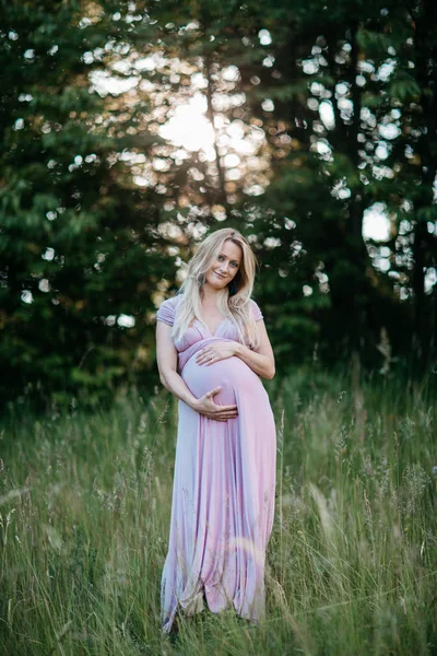 Вид спереди на счастливую беременную женщину в летнем платье, трогающую её живот . — стоковое фото