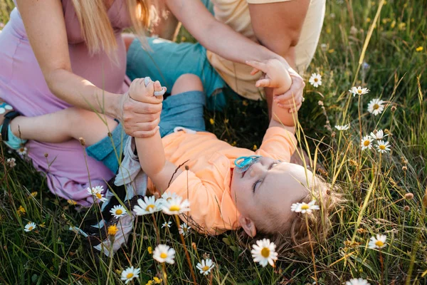 Un bambino piccolo sdraiato in un campo di margherite che gioca con i suoi genitori . — Foto Stock