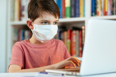 Coronavirus zamanında yüz maskesi takan çocuk evde öğreniyor. Cerrahi maske takan genç öğrenci ödevini yapıyor..