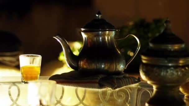 Традиционный металлический горшок и стаканы с парящим марокканский чай на восточном стиле стеклянный стол, Midshot, ночной свет — стоковое видео
