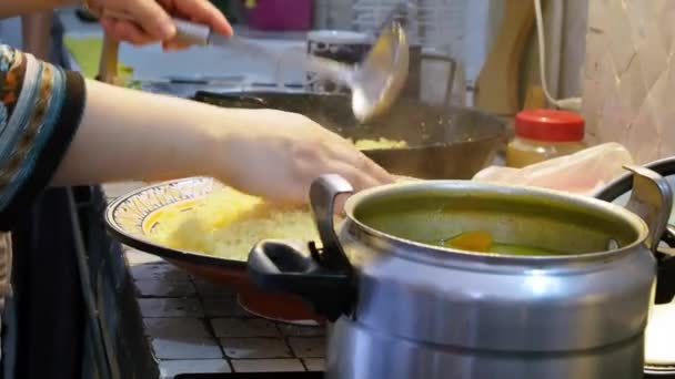 Mulher marroquina está cozinhando comida tradicional marroquina. Chef está colocando Cous Cous de uma panela para uma placa com uma concha e formá-lo com as mãos. Fecha. Tânger, Marrocos . — Vídeo de Stock