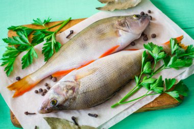 Rustik kesme tahtası ile taze otlar ve baharatlar yeşil ahşap masa üzerinde iki çiğ levrek