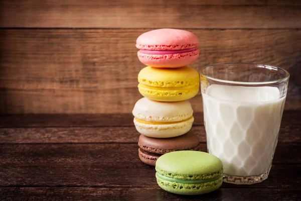Macarons coloridos e vidro de leite no fundo de madeira escura — Fotografia de Stock